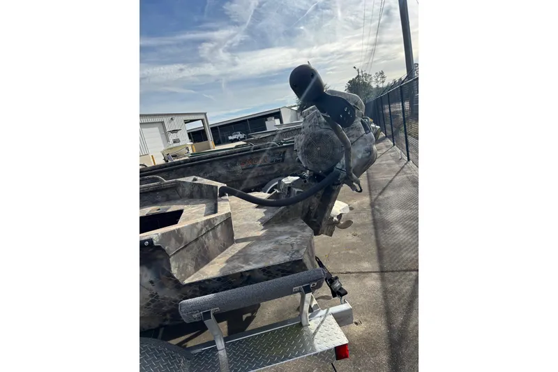 Slide: The Image of 2023 Excel 1754 Shallow Water F4 boat with camo design, parked outdoors. - 16
