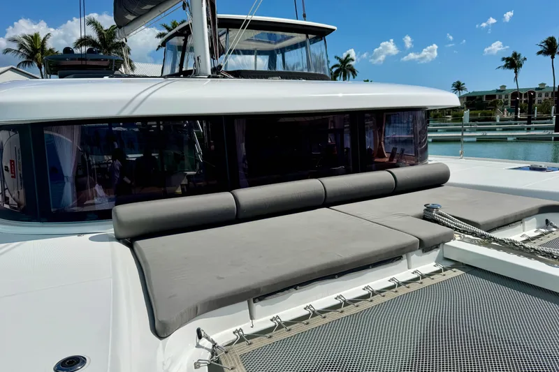 Slide: The Image of 2017 Lagoon 42 catamaran with sunbathing area, docked in a tropical marina setting. - 2