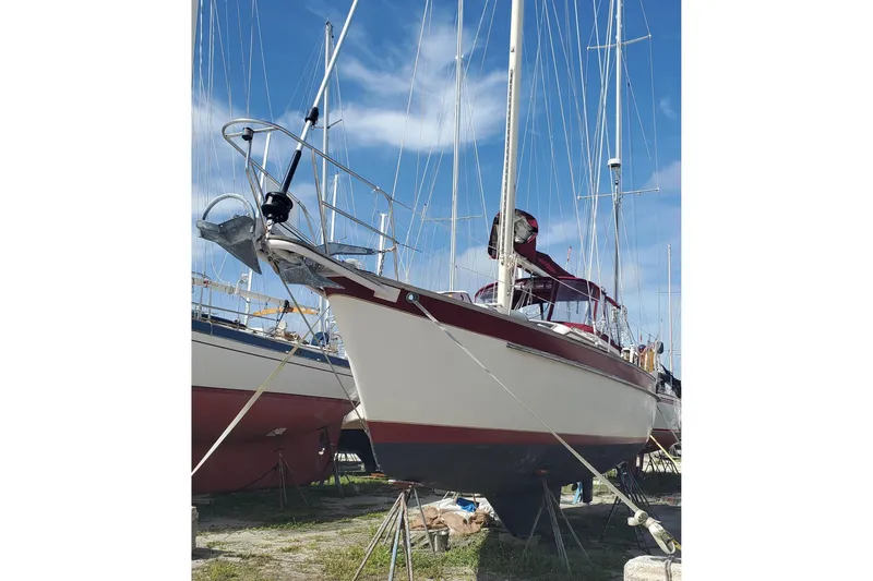 Slide: The Image of 1987 Irwin 38 Mk II sailboat on land, with red and white hull, clear sky background. - 4