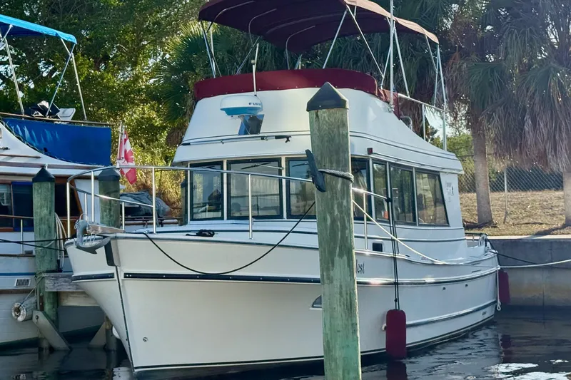 Slide: The Image of 2002 Camano Troll boat docked, featuring a white hull and red canopy, surrounded by trees. - 2