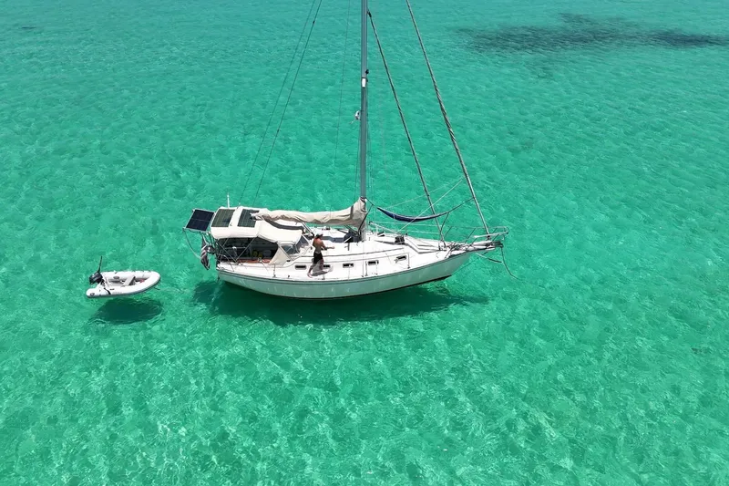 The Image of Sailboat Island Packet 32 (1994) anchored in clear turquoise water with a small dinghy. - 1