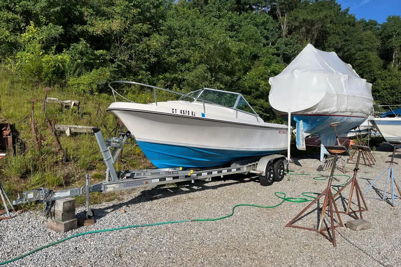 Slide: The Image of 1986 Medeiros Limestone 20 Cuddy Cabin on trailer, parked outdoors near covered boat. - 4