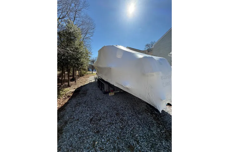 Slide: The Image of 2015 Regulator 28 Forward Seating boat covered, parked on gravel under clear sky. - 12