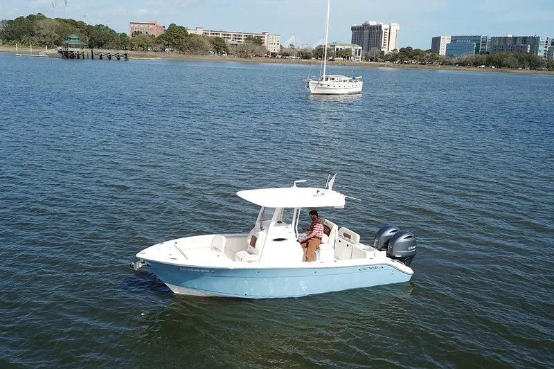 The Image of 2020 Cobia 240 Center Console boat on calm water with cityscape background. - 1