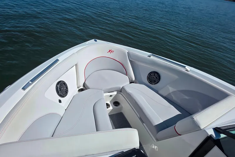 Slide: The Image of 2018 MasterCraft XT23 boat interior with white seating and red accents on calm water. - 16
