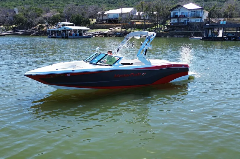 Slide: The Image of 2018 MasterCraft XT23 boat on a serene lake with houses in the background. - 4