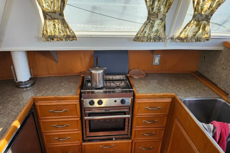 Slide: The Image of Compact kitchen in a 1987 Custom Weld Exploration boat with stove, sink, and floral curtains. - 15