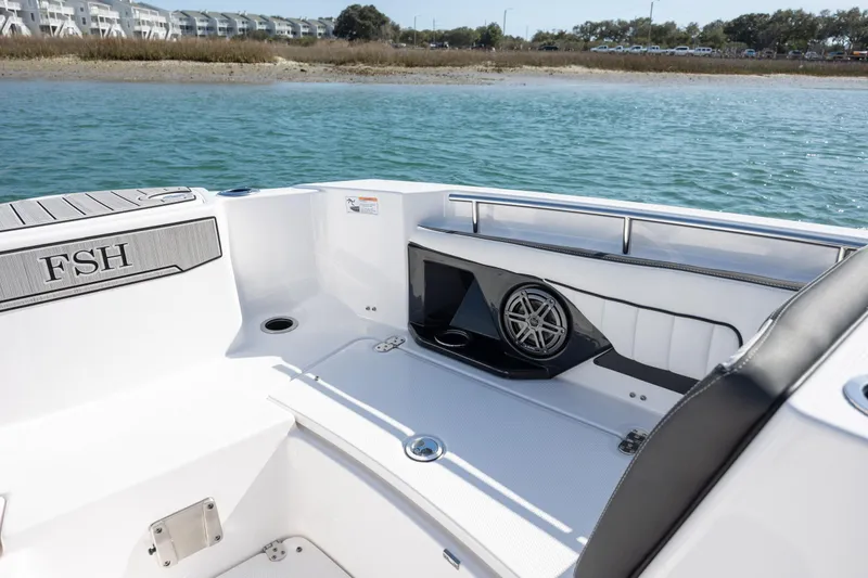 Slide: The Image of 2023 Yamaha Boats 255 FSH Sport E interior with speaker, white seating, and water view. - 12