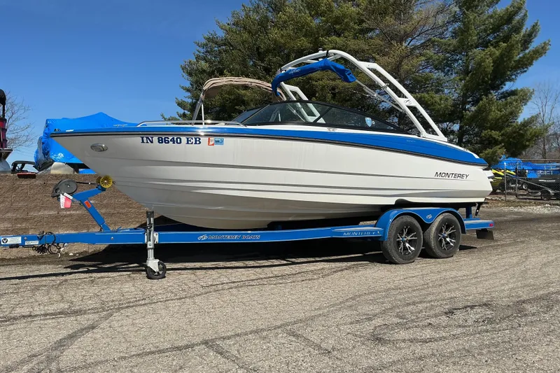 The Image of 2018 Monterey 224FS boat on trailer, parked outdoors, with blue accents and trees in background. - 1