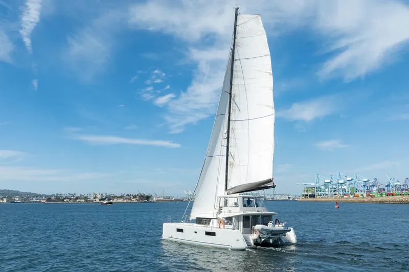 Slide: The Image of 2022 Lagoon 52 F catamaran sailing in a harbor under a clear blue sky. - 94