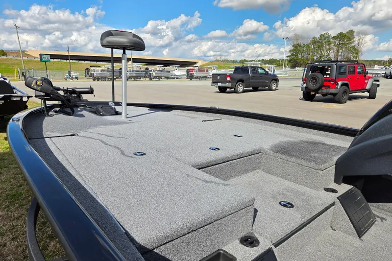 Slide: The Image of 2025 Tracker Savage 215 boat deck with trolling motor, parked in a lot under a blue sky. - 9