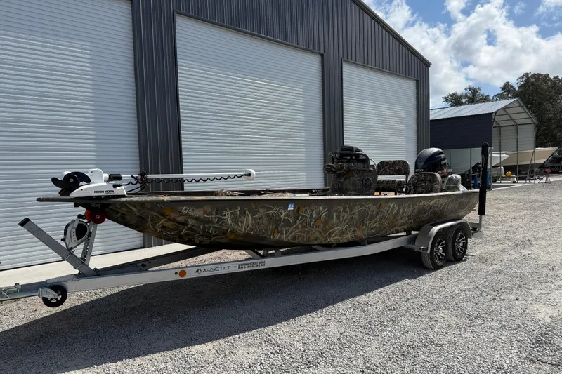 Slide: The Image of 2022 War Eagle 2170 Blackhawk boat on trailer, camo design, parked outside metal building. - 2