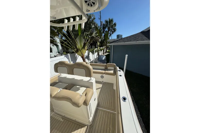 Slide: The Image of 2018 Key West 239 FS boat interior with tan seating and deck, surrounded by palm trees. - 7