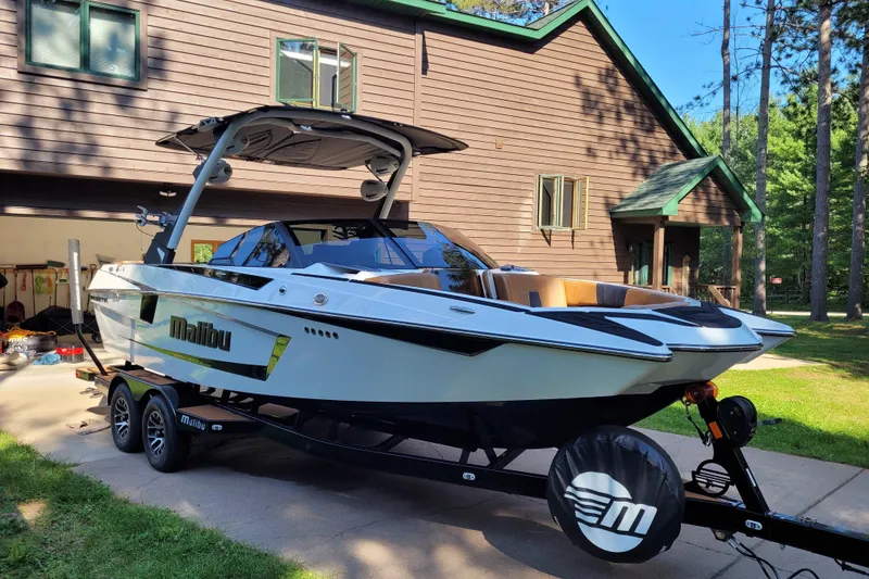 Slide: The Image of 2023 Malibu Wakesetter 23 MXZ boat on trailer, parked near a wooden house. - 10