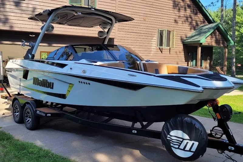 Slide: The Image of 2023 Malibu Wakesetter 23 MXZ boat on trailer, parked near a house. - 2