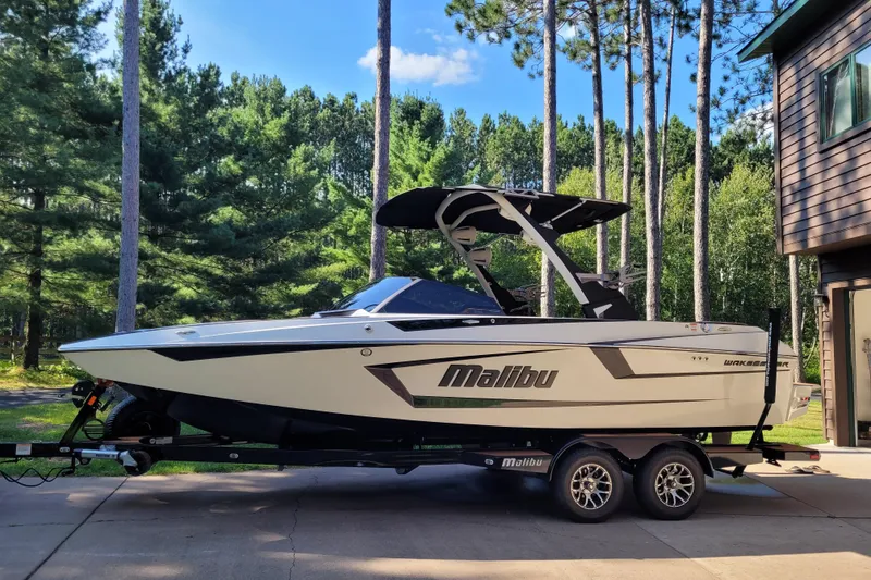 Slide: The Image of 2023 Malibu Wakesetter 23 MXZ boat on trailer, surrounded by trees and a house. - 8