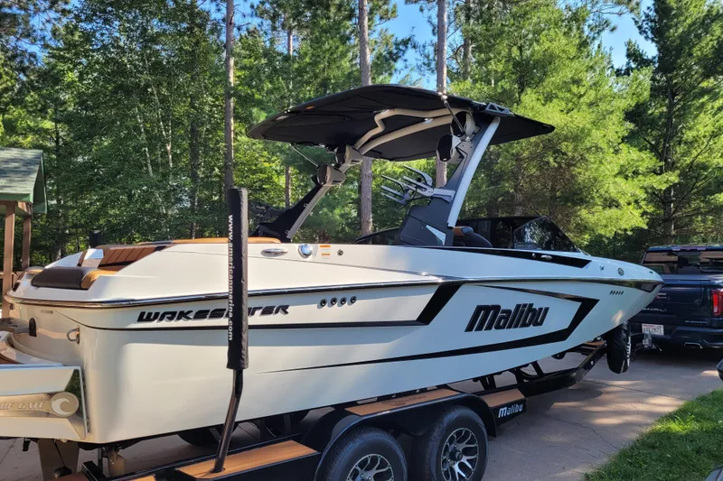 Slide: The Image of 2023 Malibu Wakesetter 23 MXZ boat on trailer, surrounded by trees. - 9