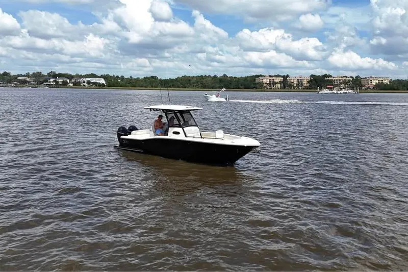 Slide: The Image of 2026 Scout 277 LXF boat cruising on a calm river under a partly cloudy sky. - 18