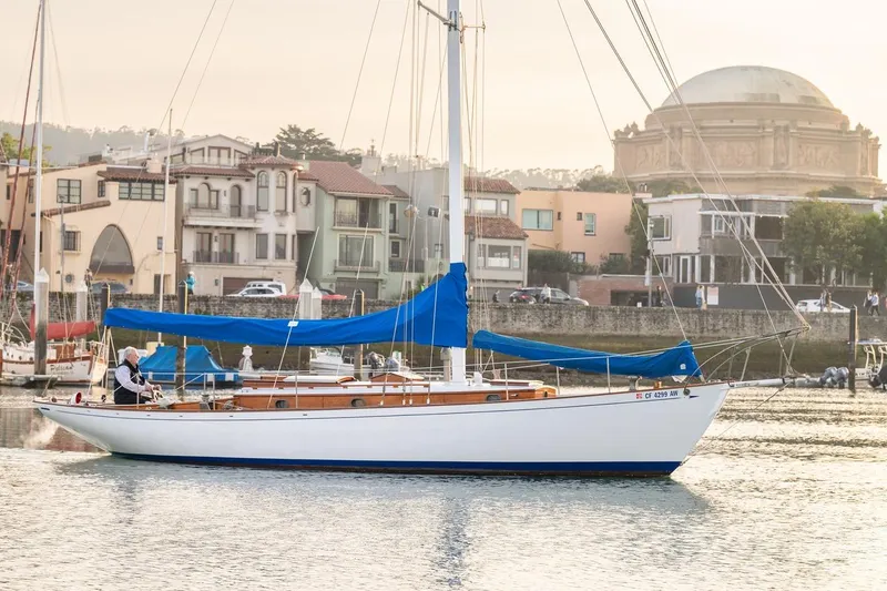 Slide: The Image of Vintage 1938 Philip Rhodes Cutter sailboat with blue sails in a scenic harbor setting. - 10