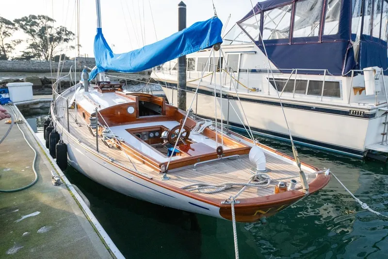 Slide: The Image of 1938 Philip Rhodes Cutter sailboat docked, featuring classic wooden design and blue sail cover. - 17