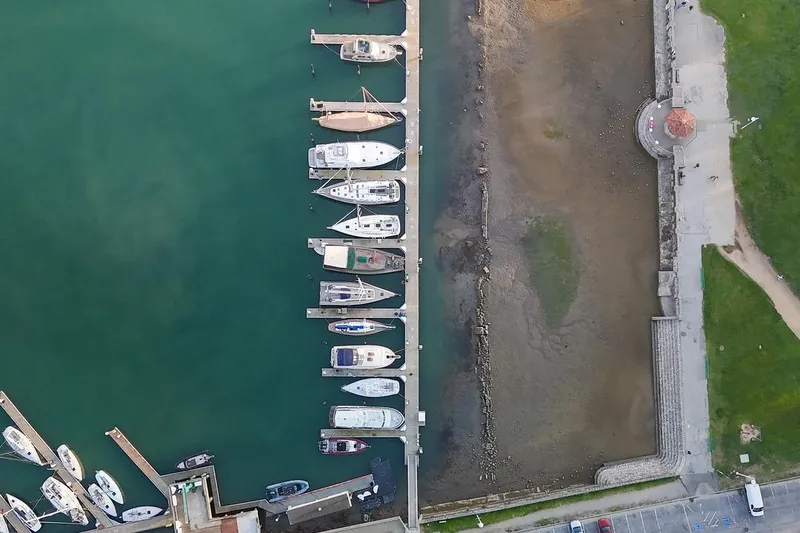Slide: The Image of Aerial view of marina with boats, including a 1938 Philip Rhodes Cutter, docked alongside a promenade. - 71