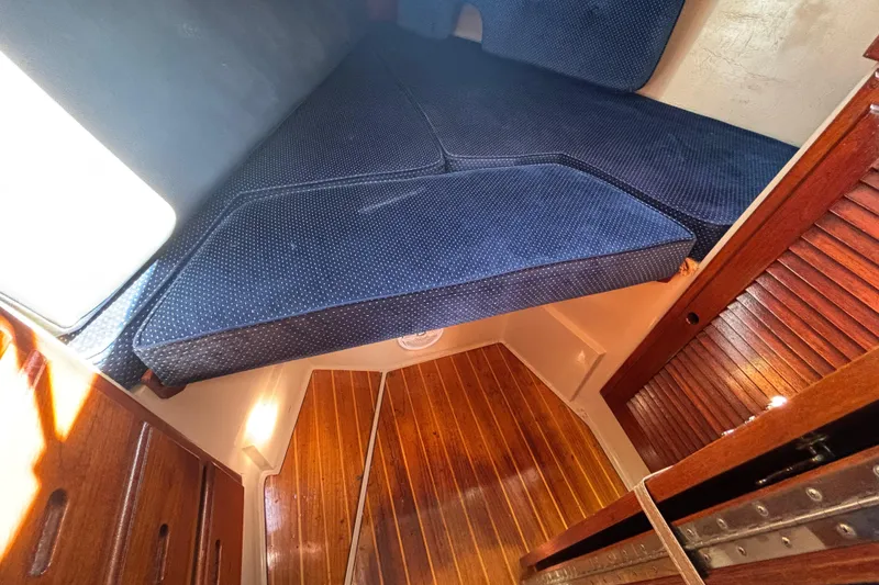 Slide: The Image of 1988 Catalina 34 sailboat interior with blue cushioned V-berth and wooden flooring. - 15