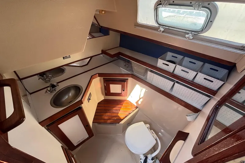 Slide: The Image of 1988 Catalina 34 yacht bathroom with sink, toilet, storage bins, and wooden accents. - 19