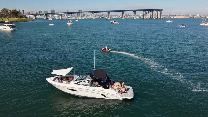 The Image of A 2019 Cruisers Yachts 338 CX South Beach Bow Rider on calm water. Several boats nearby, with a bridge in the background. - 3