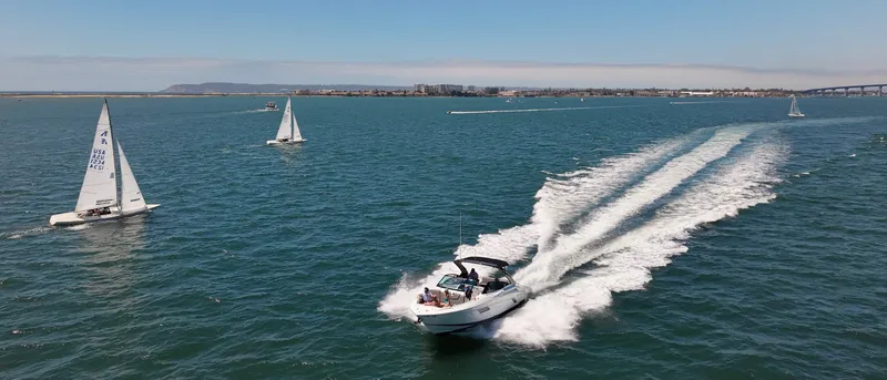 Slide: The Image of A white motorboat speeds across blue water, surrounded by sailboats and a bridge in the background. - 47