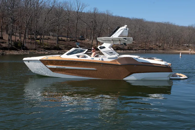 Slide: The Image of 2026 MasterCraft X24 boat on a calm lake with wooded shoreline. - 50