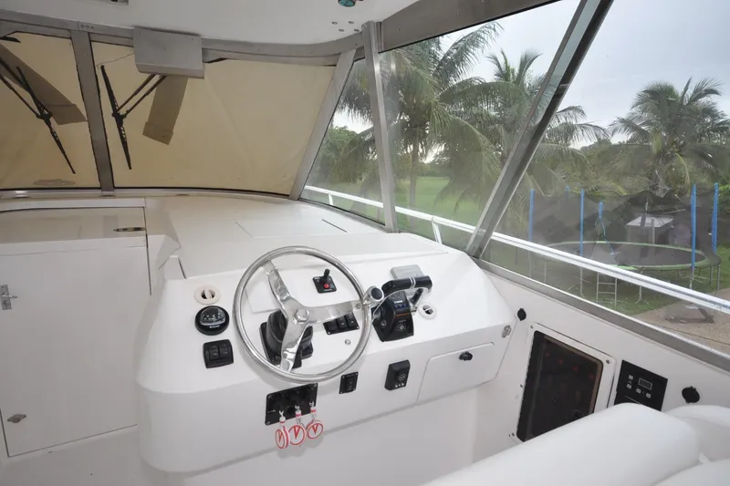 Slide: The Image of 2009 Intrepid 430 Sport Yacht helm with steering wheel and controls, overlooking palm trees. - 2