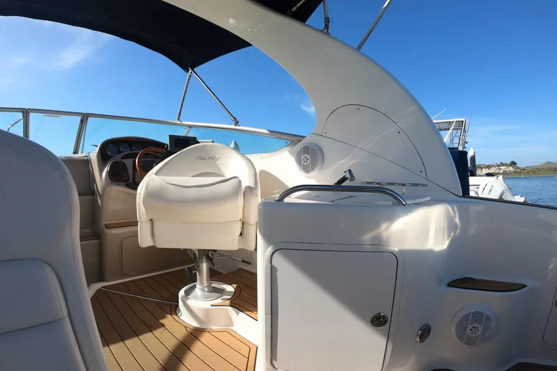 Slide: The Image of 2004 Sea Ray Sundancer 280 cockpit with helm, white seating, and wood flooring under blue sky. - 22