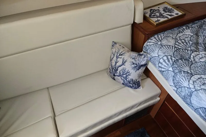 Slide: The Image of 2009 Mainship Pilot 31 interior with white seating, nautical pillow, and shell-patterned bedding. - 20