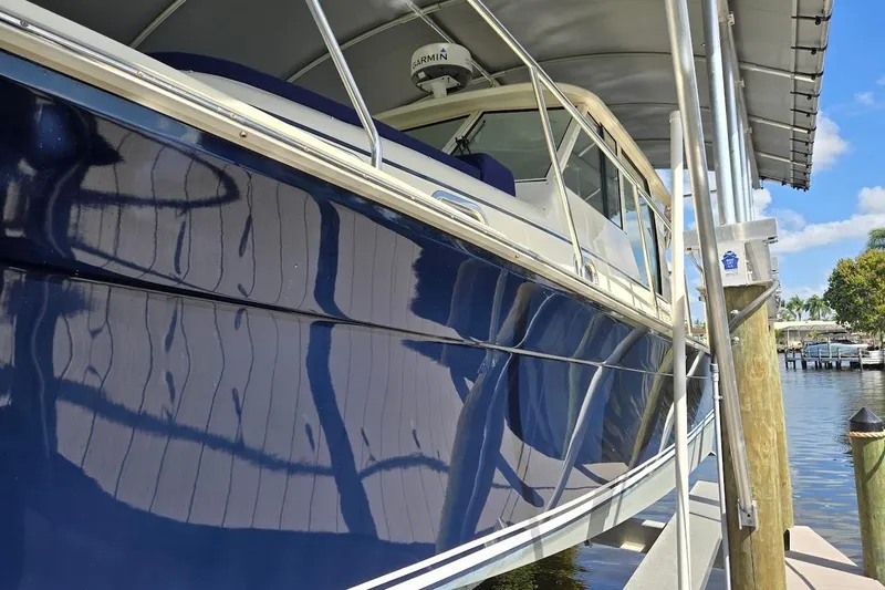 Slide: The Image of 2009 Mainship Pilot 31 boat docked under a canopy, reflecting water and sky. - 80
