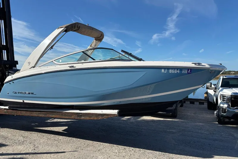 Slide: The Image of 2021 Regal 23 OBX boat in blue, parked on a trailer under a clear sky. - 7