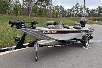 Slide: The Image of 2002 Tracker Pro Team 165 boat on trailer, parked outdoors, with motor and fishing equipment. - 7