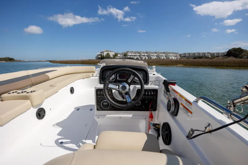 Slide: The Image of 2019 Hurricane SunDeck Sport 201 OB boat interior with steering wheel, beige seating, and water view. - 11