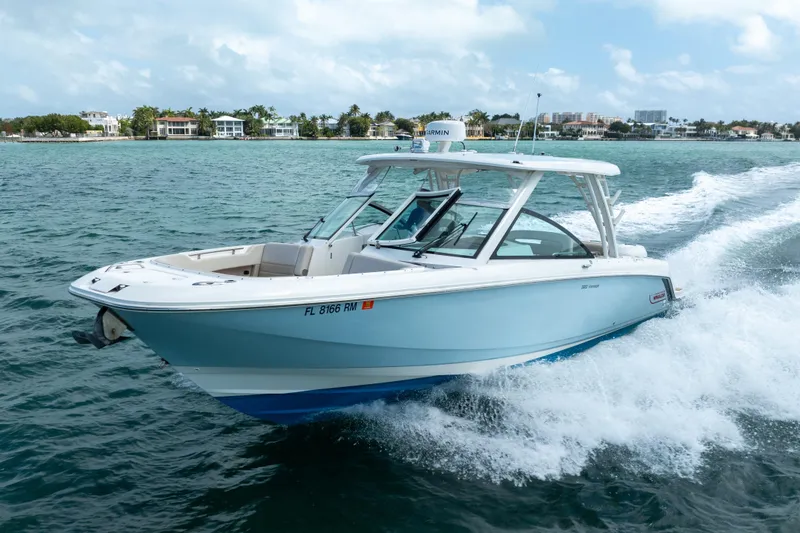 Slide: The Image of 2018 Boston Whaler 320 Vantage cruising on open water near coastal homes. - 0