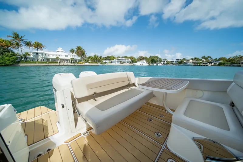 Slide: The Image of 2018 Boston Whaler 320 Vantage boat interior with seating and table, overlooking scenic waterfront. - 23