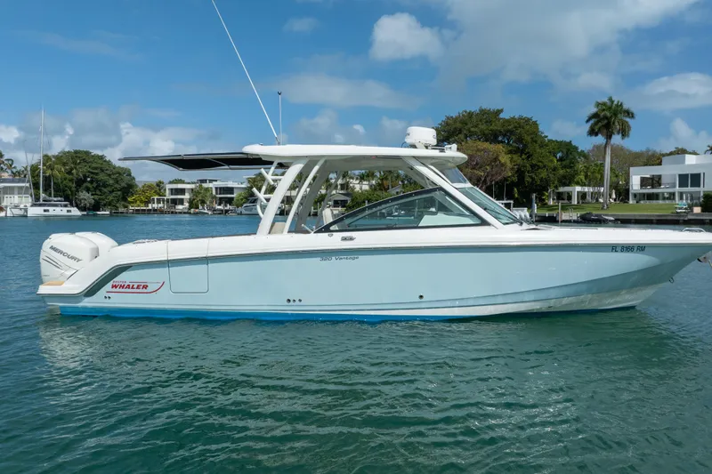 Slide: The Image of 2018 Boston Whaler 320 Vantage boat on calm water, with modern waterfront homes in the background. - 8