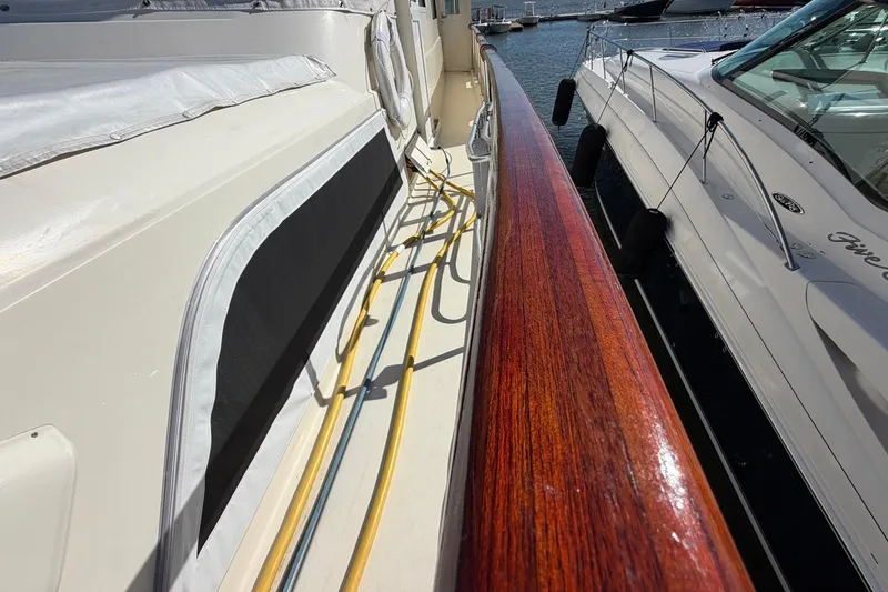 Slide: The Image of 1987 Hatteras 58 Motor Yacht docked, showcasing polished wood railing and deck details. - 12