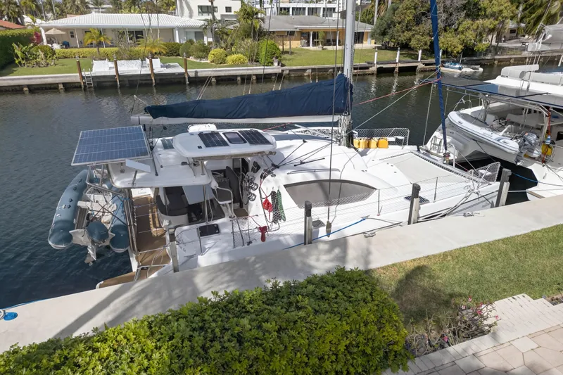 Slide: The Image of 2012 Leopard 39 catamaran docked, featuring solar panels and a dinghy, in a serene canal setting. - 14