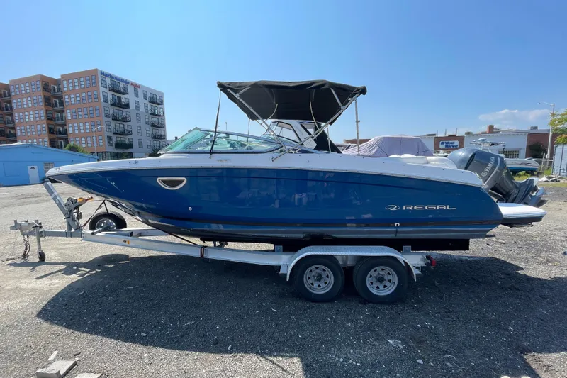 Slide: The Image of 2018 Regal 26 OBX boat on trailer, blue hull, parked outdoors near buildings. - 1