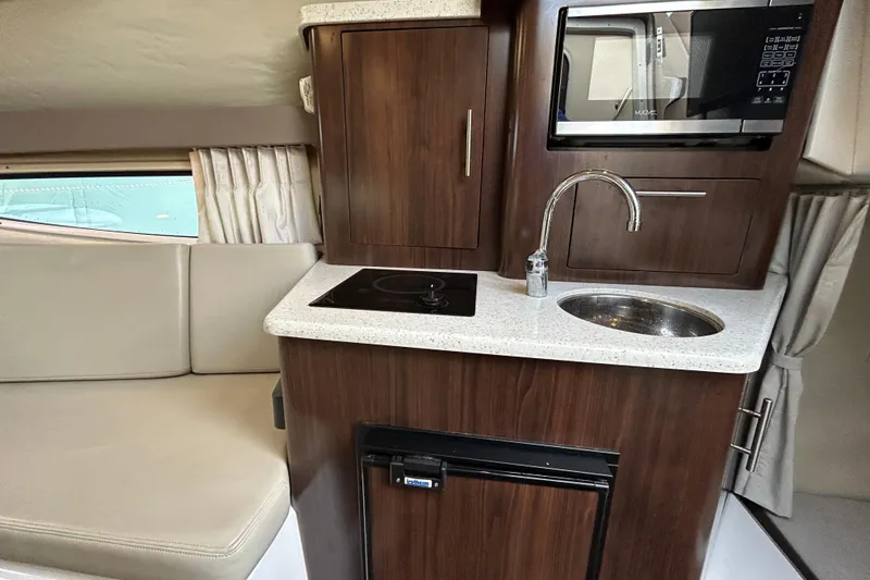 Slide: The Image of 2017 Regal 28 Express boat interior with kitchenette, featuring sink, stove, and microwave. - 13
