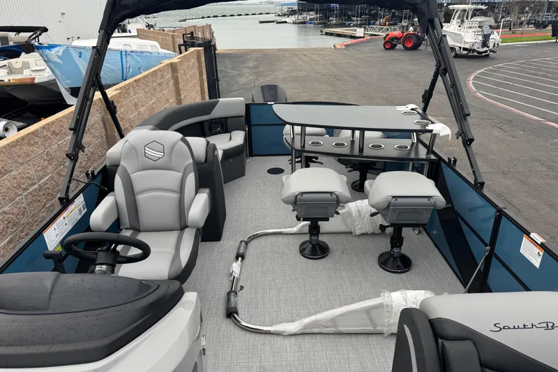 Slide: The Image of 2026 South Bay S222E pontoon boat interior with seating and table, docked at marina. - 12