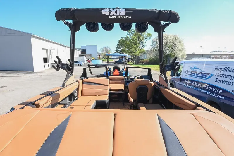 Slide: The Image of 2023 Axis A225 boat interior with tan seating, wakeboard tower, and marine service van nearby. - 12
