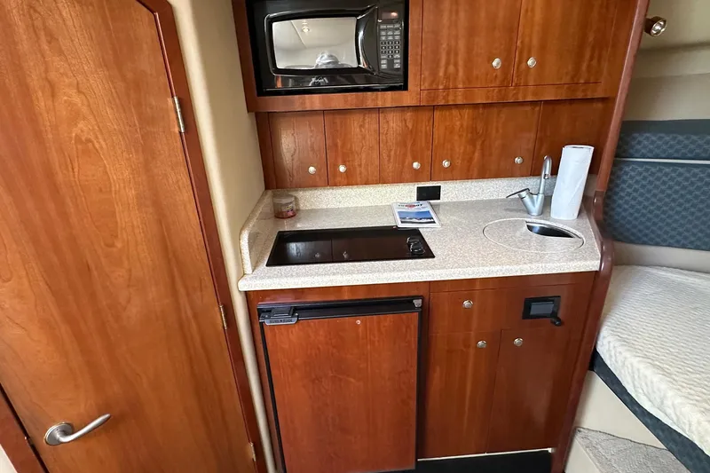 Slide: The Image of 2006 Rampage 33 Express boat interior with kitchenette, featuring microwave, sink, and wooden cabinetry. - 15