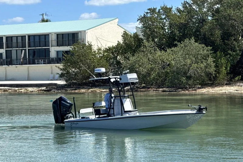 The Image of 2026 Yellowfin 24 Bay CE boat on calm water near a building and trees. - 1