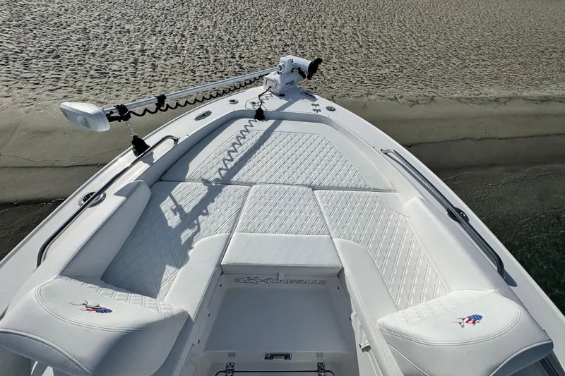 Slide: The Image of 2025 Crevalle 24 HCO boat with white cushioned seating and trolling motor on sandy shore. - 10