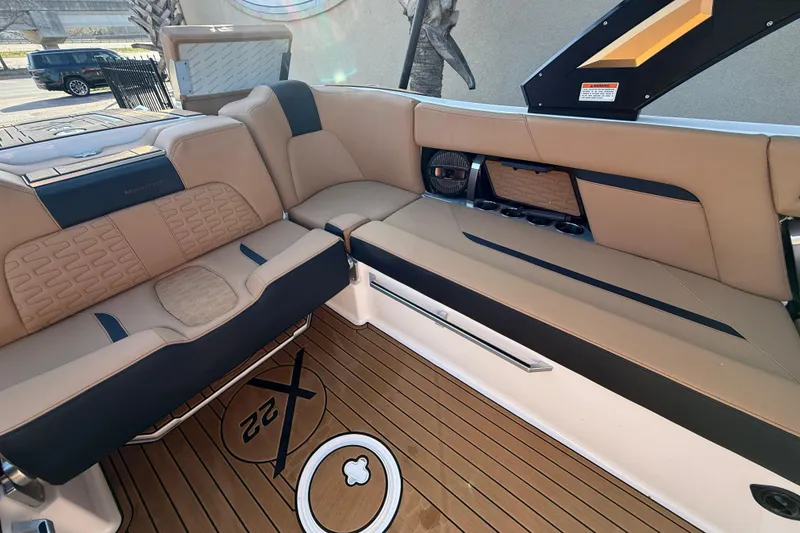 Slide: The Image of 2023 MasterCraft X22 boat interior with tan and black seating, teak flooring, and cup holders. - 15